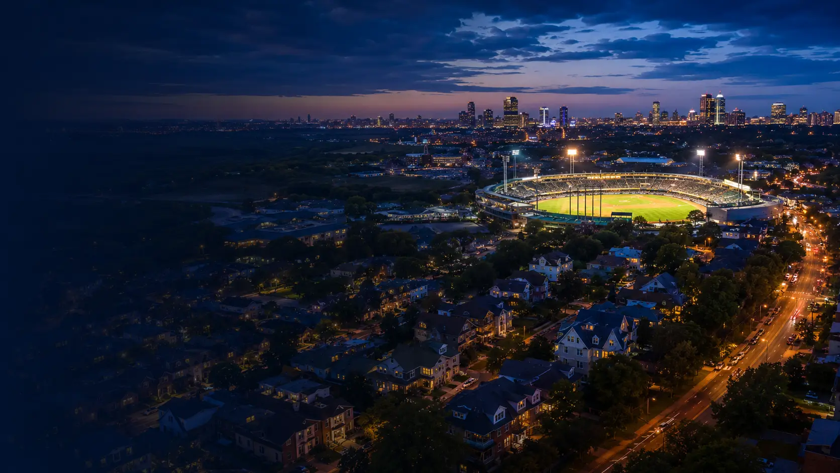A blue-hour American city, residential neighborhoods, and an illuminated baseball stadium